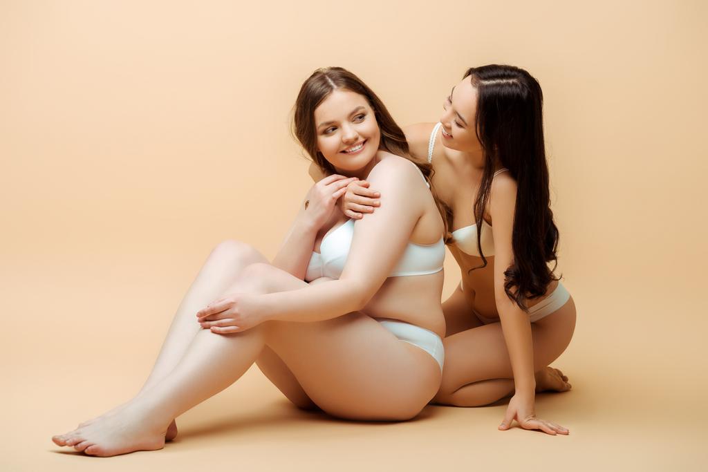 aziatische meisje knuffelen gelukkig overgewicht vrouw in ondergoed terwijl zitten op beige, lichaam positief concept  - Foto, afbeelding