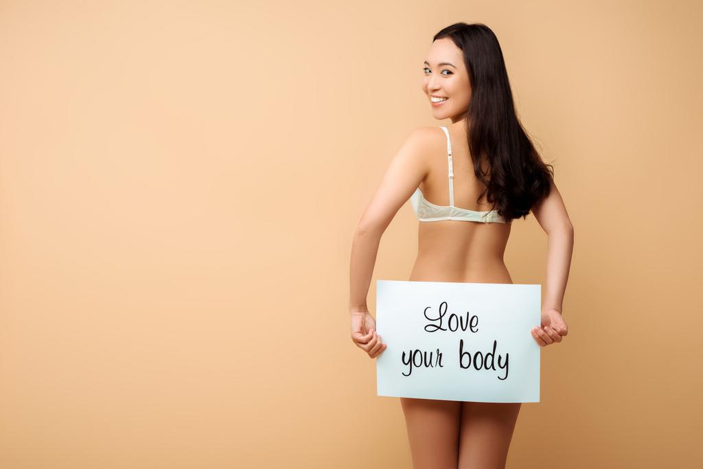 šťastná asijská dívka drží plakát s láskou vaše tělo písmena izolované na béžové  - Fotografie, Obrázek