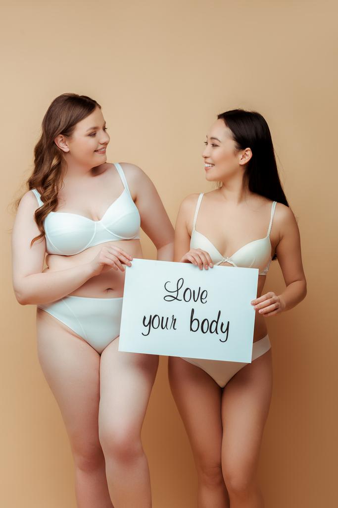 alegre multicultural niñas en ropa interior celebración cartel con amor su cuerpo letras aislado en beige, cuerpo concepto positivo
  - Foto, imagen
