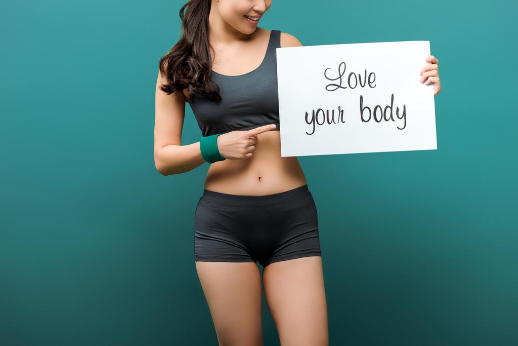 Oříznutý pohled sportovkyně usmívající se a ukazující na plakát s láskou vaše tělo nápisy na zeleném pozadí - Fotografie, Obrázek