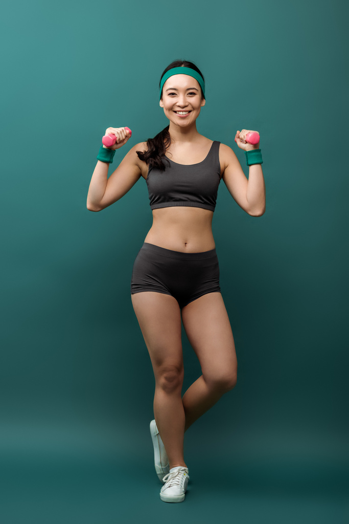 Halterli mutlu Asyalı sporcu kadın eğitimi. Gülümsüyor ve yeşil arka plandaki kameraya bakıyor. - Fotoğraf, Görsel