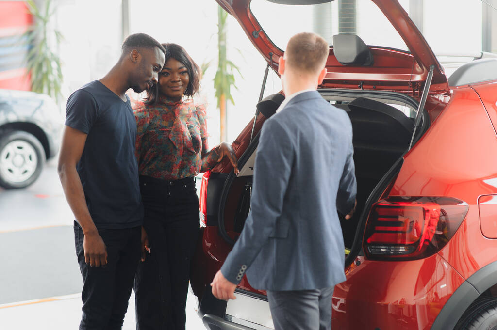 vendedor mostrando coche nuevo a pareja africana en sala de exposición
 - Foto, Imagen