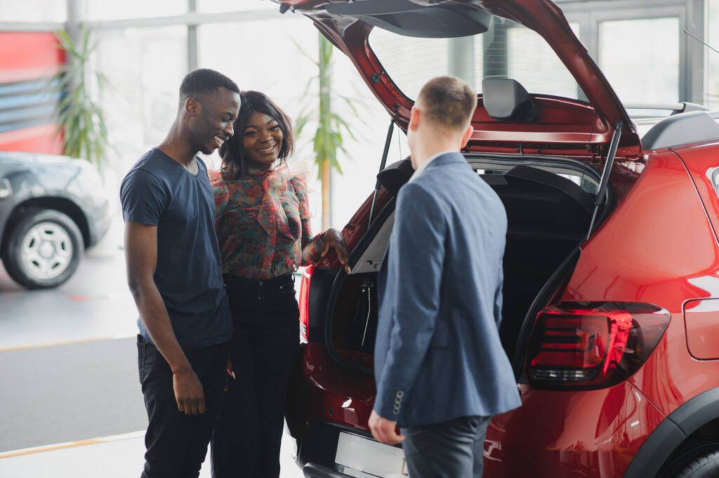 Afrikai amerikai család az autókereskedésben. Az eladó megmutatja az új piros autó csomagtartóját.. - Fotó, kép