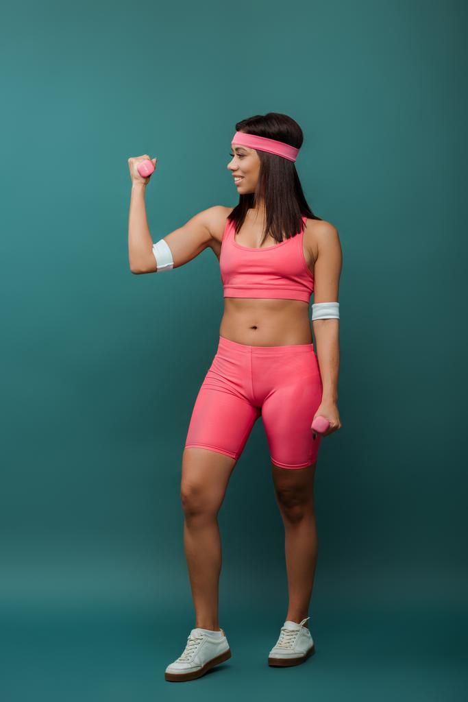 Afroamerikanische Sportlerin lächelt und blickt auf Hantel auf grünem Hintergrund - Foto, Bild
