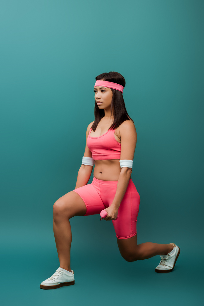 緑の背景にダンベルと肺を行うアフリカ系アメリカ人のスポーツ女性 - 写真・画像