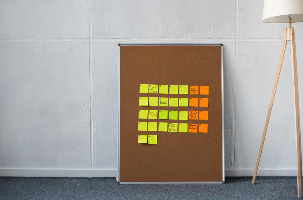 Brown board with yellow and orange sticky notes and floor lamp near wall - Photo, Image