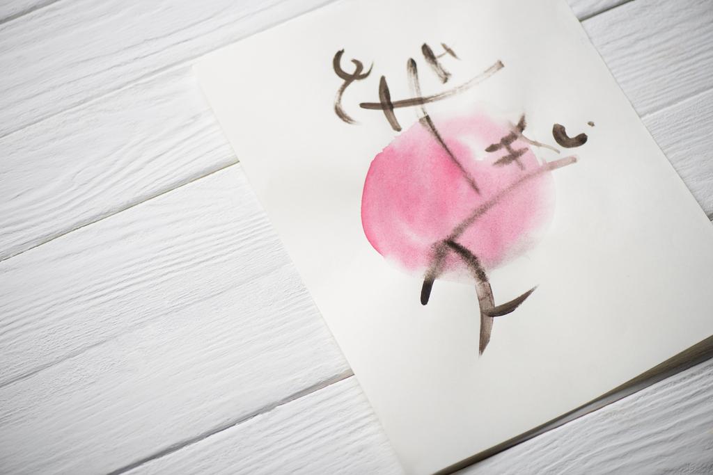 High angle view of paper with japanese painting with hieroglyphs on pink circle on wooden background - Photo, Image