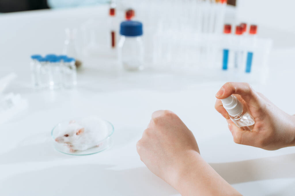 przycięty widok naukowca rozpylającego środki antyseptyczne na dłonie w pobliżu probówek i pojemników z lekami - Zdjęcie, obraz
