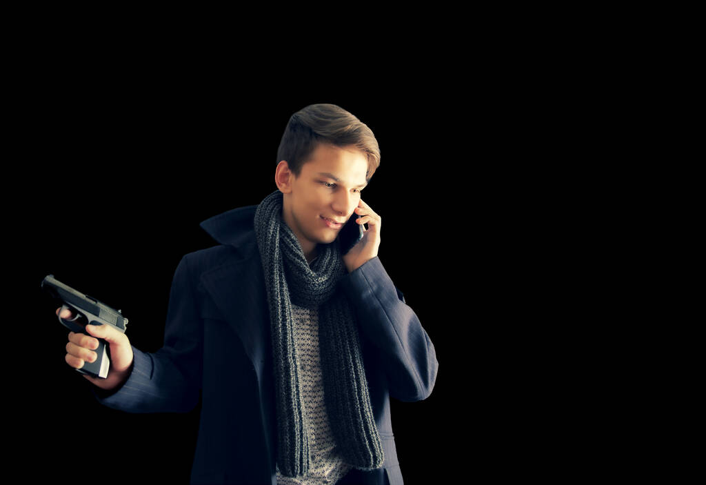 Salaperäinen soluttautuja nuori mies-gangsteri aseen kanssa ja yllään tumma takki on ikävä puhelinkeskustelu eristetty mustalla taustalla
 - Valokuva, kuva