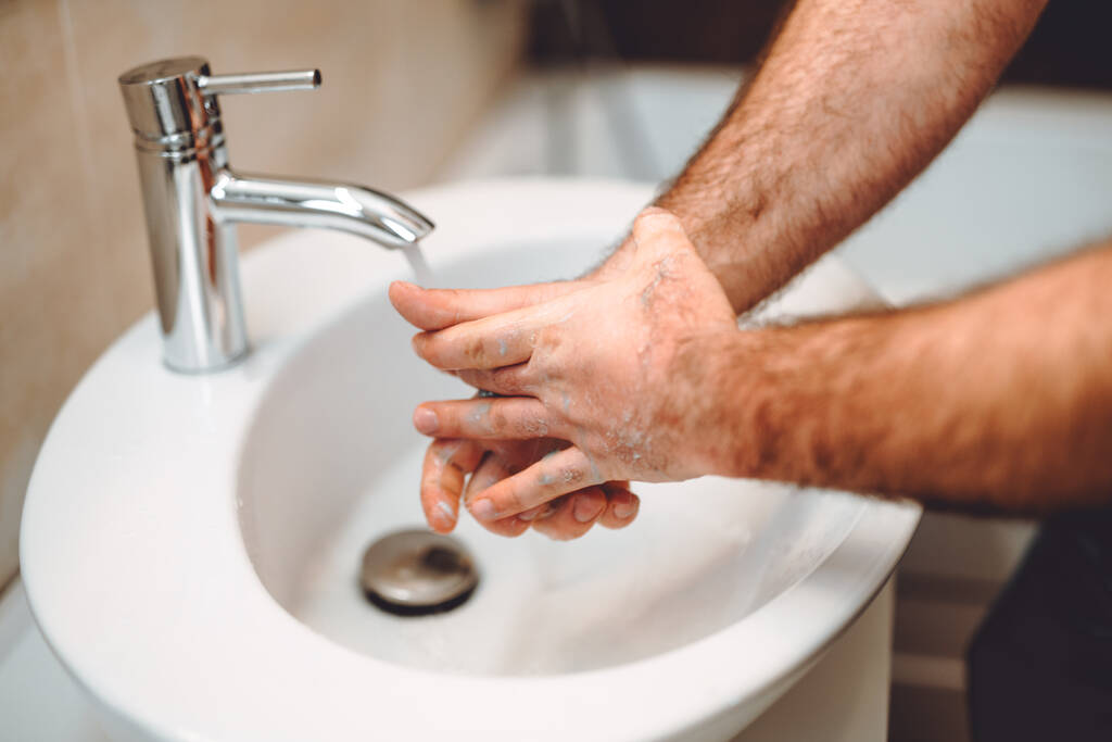 Jovem homem adulto lavando as mãos em casa usando desinfetante e gel, água quente da torneira e cosméticos de limpeza
 - Foto, Imagem