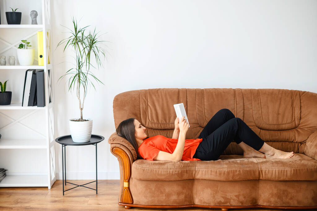 Mulher se deita no sofá e lê um livro
 - Foto, Imagem