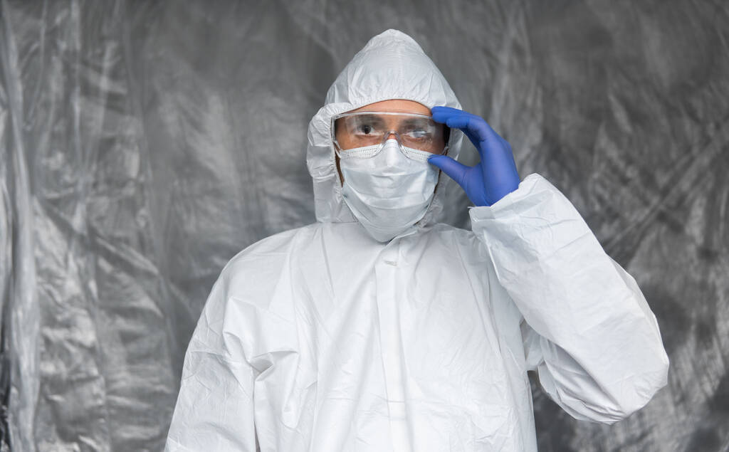 Beyaz koruyucu giysili, maskeli, gözlüklü ve lastik eldivenli doktor koronavirüs salgını tehdidi altındaki insanlara yardım etmeye hazır. Salgın, Coronavirus covid 19 salgını. Solunum cihazındaki doktor.. - Fotoğraf, Görsel