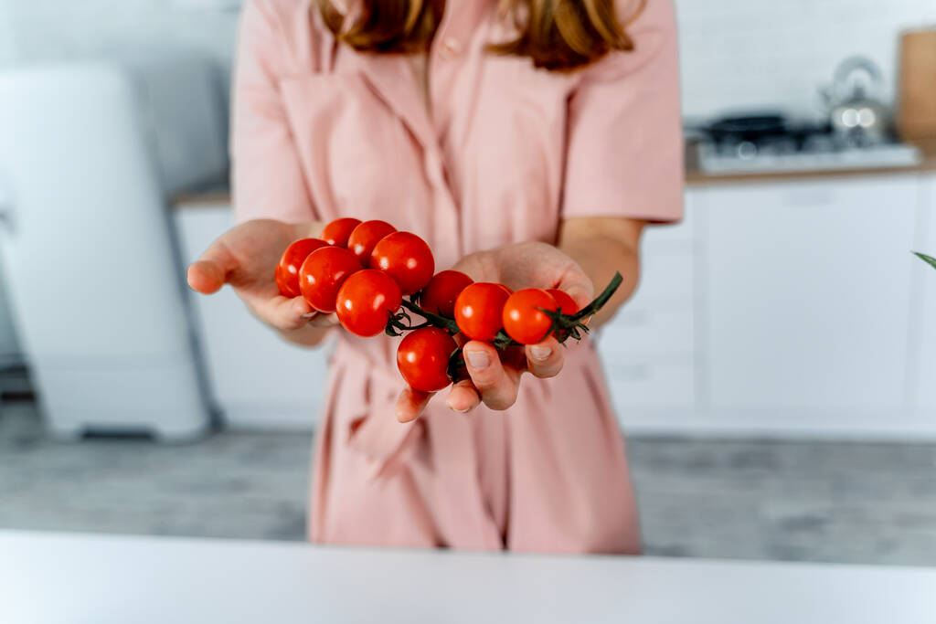 Домогосподарка тримає стиглі вишневі помідори в руках. Кухонний фон. Рожева сукня на жінці. Концепція домашнього харчування
. - Фото, зображення