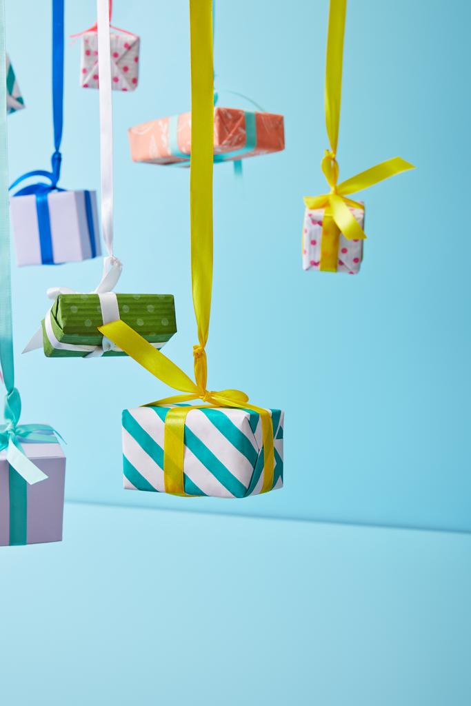 feestelijke kleurrijke geschenkdozen opknoping op linten op blauwe achtergrond - Foto, afbeelding