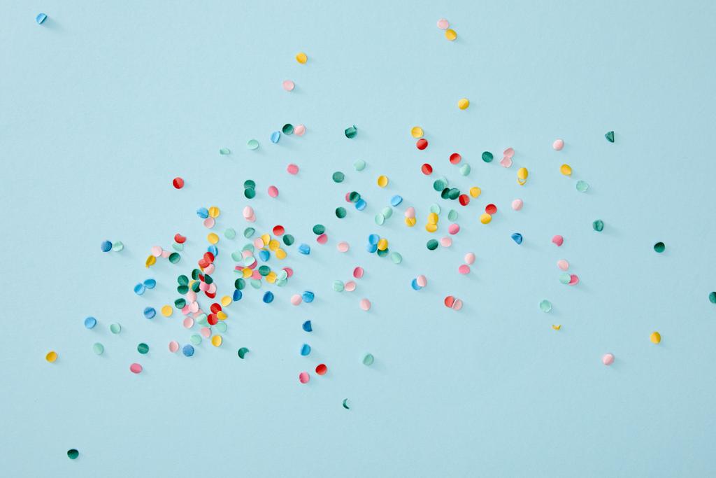 bovenaanzicht van kleurrijke confetti verspreid over blauwe achtergrond - Foto, afbeelding