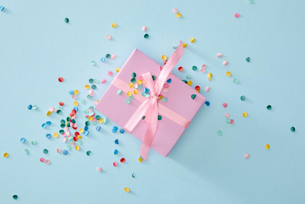 вид сверху красочные конфетти рядом с розовой коробке подарка на голубом фоне
 - Фото, изображение