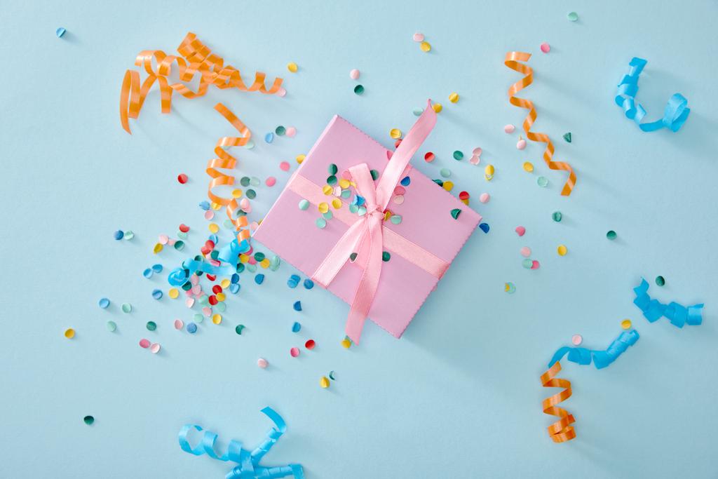 top view of colorful confetti near pink gift box on blue background - Photo, Image