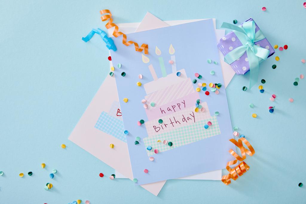 vista superior de confeti colorido cerca de tarjetas de felicitación de cumpleaños sobre fondo azul
 - Foto, imagen