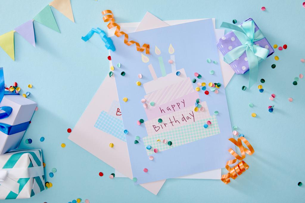 Draufsicht auf bunte Konfetti in der Nähe von Geschenkboxen und Geburtstagsgrußkarten auf blauem Hintergrund - Foto, Bild