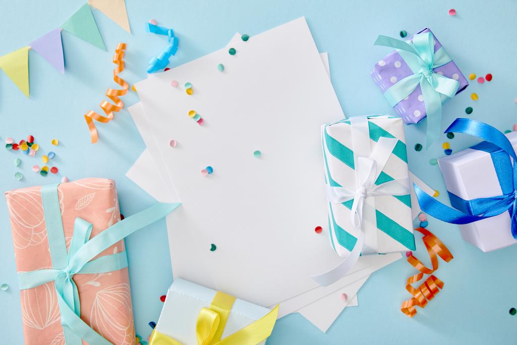 vista superior de confetes coloridos perto de papel em branco e caixas de presente no fundo azul
 - Foto, Imagem