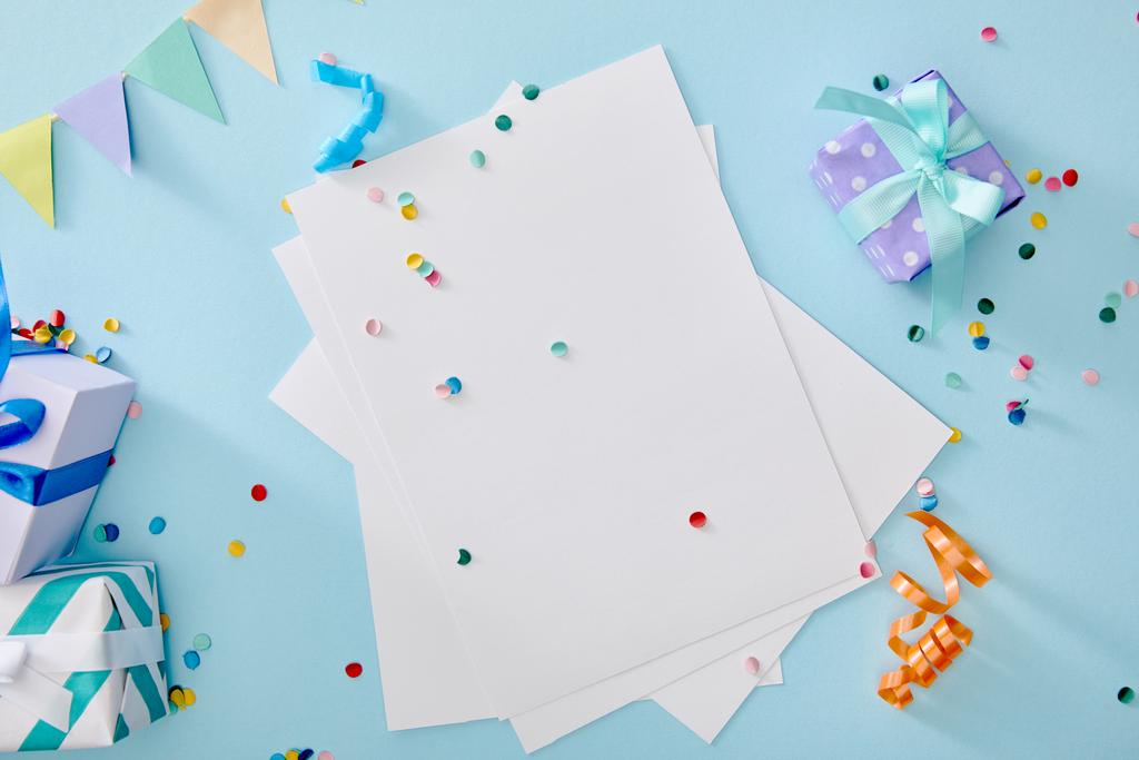 Boş kağıdın yanında renkli konfeti ve mavi arkaplanda hediye kutularının üst görünümü - Fotoğraf, Görsel