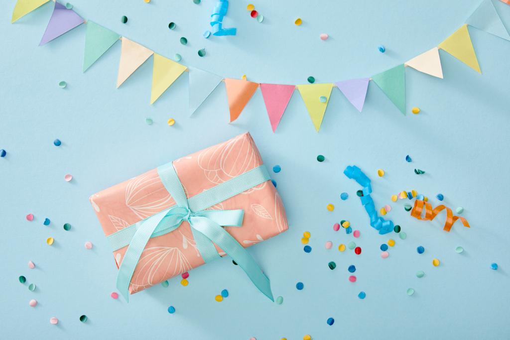 top view of colorful confetti near gift box on blue background - Photo, Image