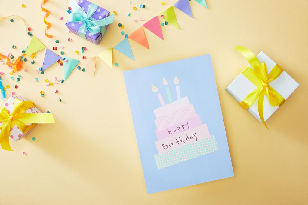 Rengarenk konfetilerin üst görüntüsü ve bej arka planda doğum günü tebrik kartı yakınında hediye kutuları - Fotoğraf, Görsel