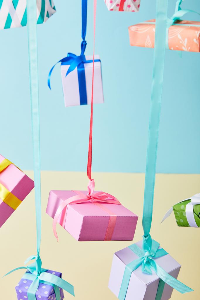 γιορτινά πολύχρωμα κουτιά δώρων που κρέμονται σε κορδέλες σε μπλε και κίτρινο φόντο - Φωτογραφία, εικόνα