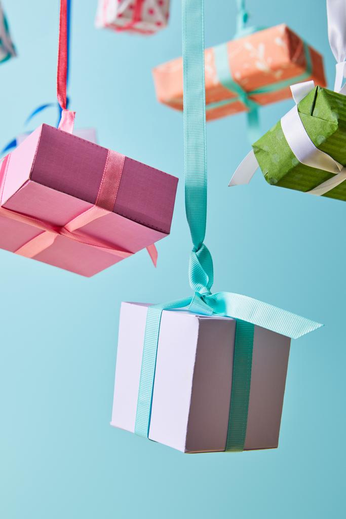 селективный фокус праздничных красочных подарочных коробок, висящих на лентах, изолированных на голубом
 - Фото, изображение