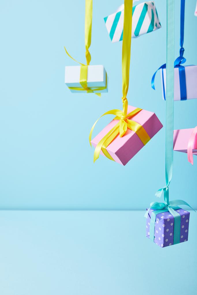 праздничные красочные подарочные коробки висят на лентах на синем фоне
 - Фото, изображение