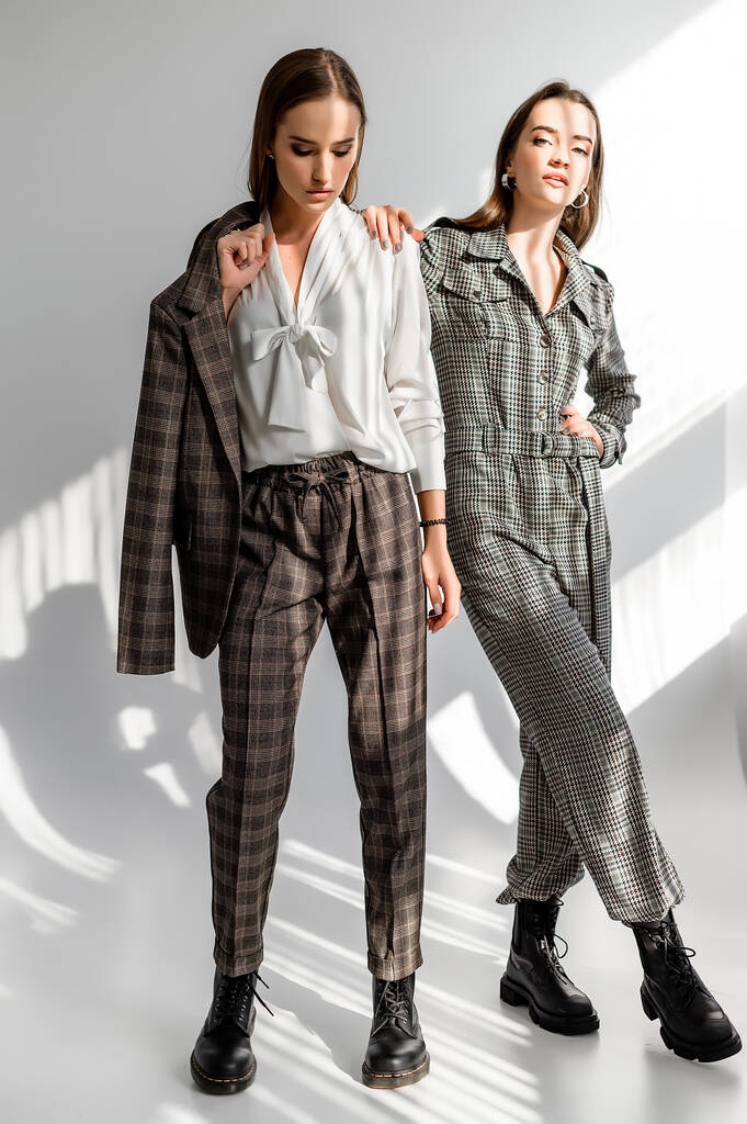 Dos chicas en traje de pantalón y un overol de cheques sobre fondo blanco
 - Foto, Imagen
