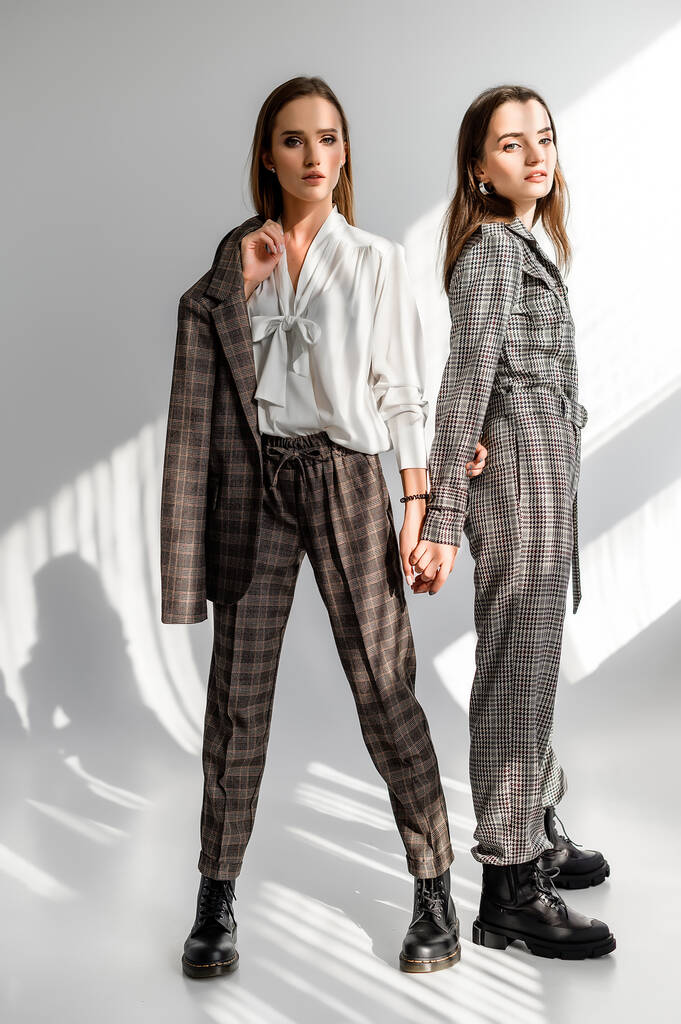 Duas meninas em um terno de calças e um macacão de cheque em um fundo branco
 - Foto, Imagem
