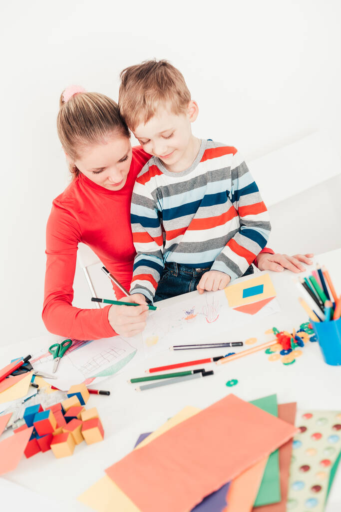 Mother and her son drawing picture together at white desk - Photo, Image