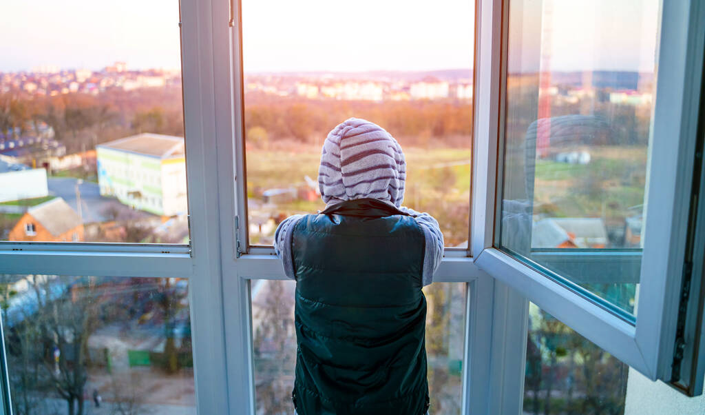 Coronavirus epidemie zelf-isolatie. De jongen blijft thuis. Geen school. Tiener staat op Balkony. Foto van achteren. - Foto, afbeelding