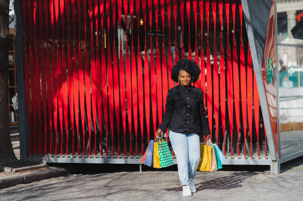 Jovem mulher afro-americana atraente compras - sacos de compras, ao ar livre, vista de rua, adequado para temas de compras de férias, entre outros
 - Foto, Imagem