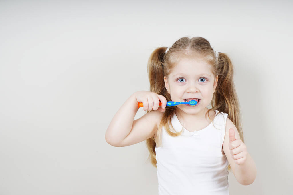 Avrupalı görünümlü küçük bir kız arka planda dişlerini fırçalıyor. Sağlıklı diş kavramı. Dişçilik - Fotoğraf, Görsel