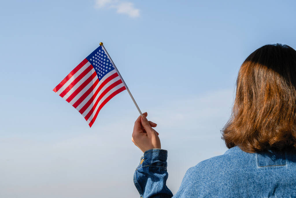 Mano donna con bandiera americana ondeggiante sul cielo blu. L'America. Stati Uniti. Concetto
 - Foto, immagini