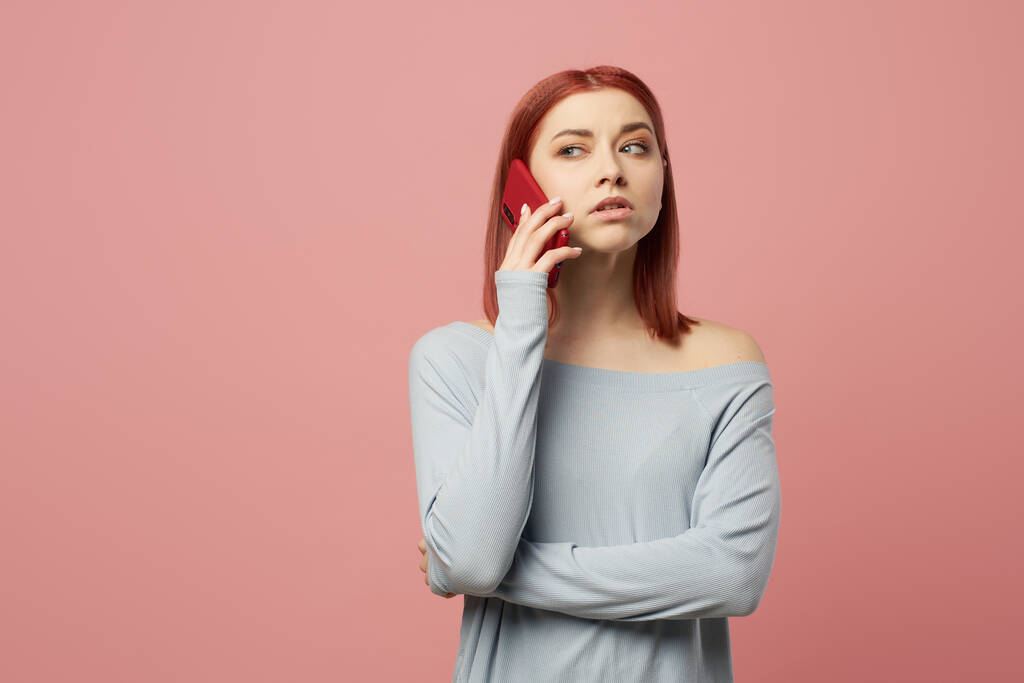 Серьезная женщина разговаривает по телефону, стоя в студии на розовом фоне
 - Фото, изображение