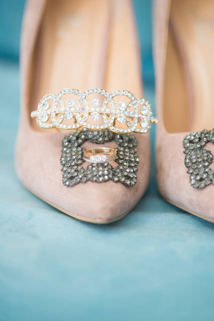 Divatos, kecses szarvasbőr magassarkú cipő, jegygyűrűk és ékszerek egy kék szarvasbőr székben. Esküvői részletek. Szépség és divat. - Fotó, kép