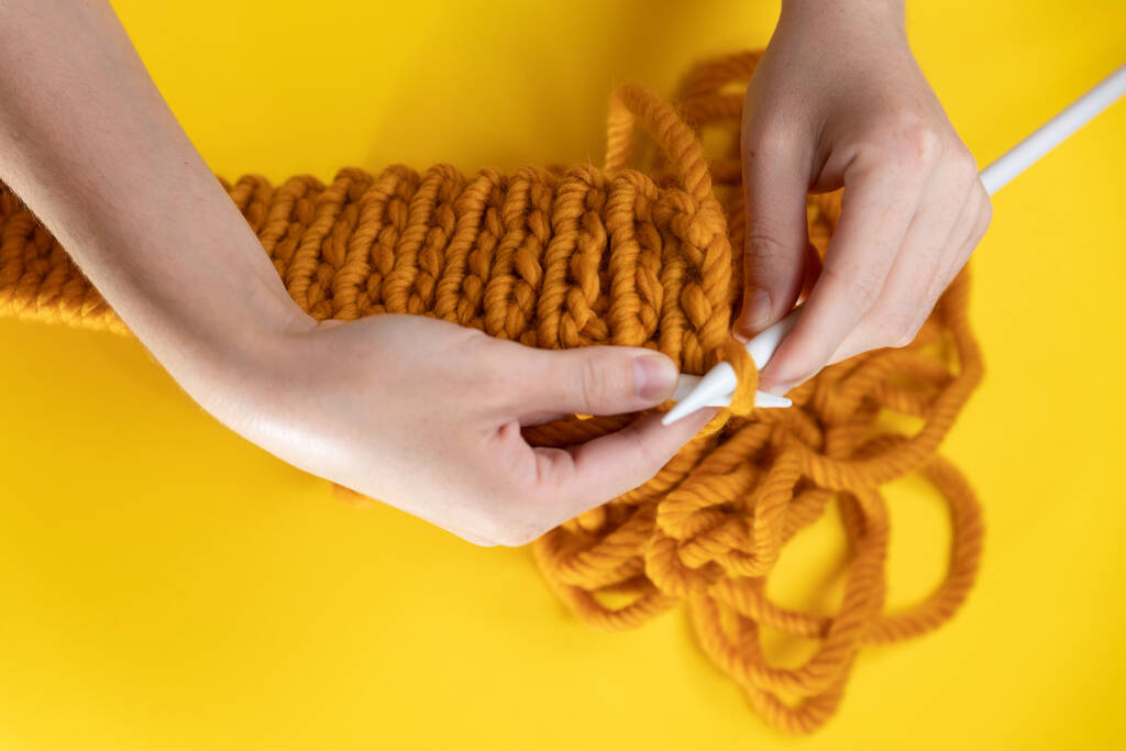 黄色の背景に黄色のウールからの女性の手ニット、トップビュー。手編み - 写真・画像