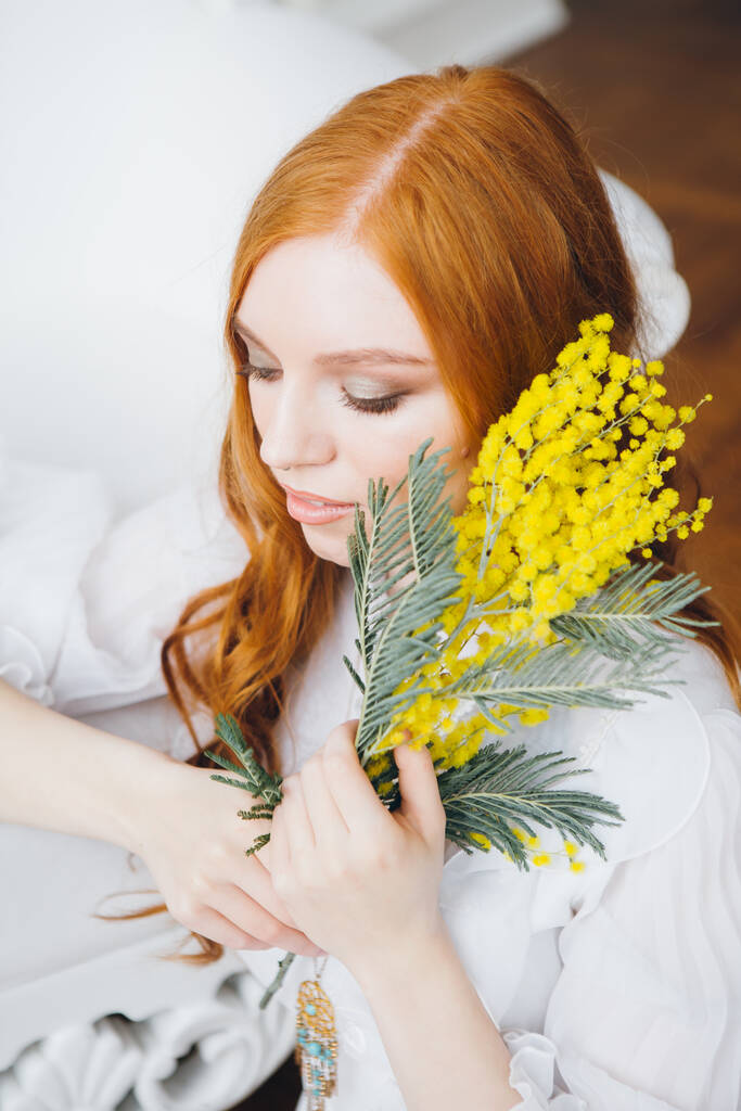 Retrato de una hermosa chica pelirroja con una Mimosa en un largo vestido blanco. Concierto de primavera. Tonificación
. - Foto, Imagen
