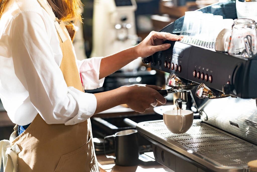 Modern kahve makinesi tarafından kahve yapan bir baristanın arka planda çalışan diğer baristalarla kahve yaparken yakın plan çekimi. Küçük işletme sahibi konsepti için kullanılıyor. - Fotoğraf, Görsel
