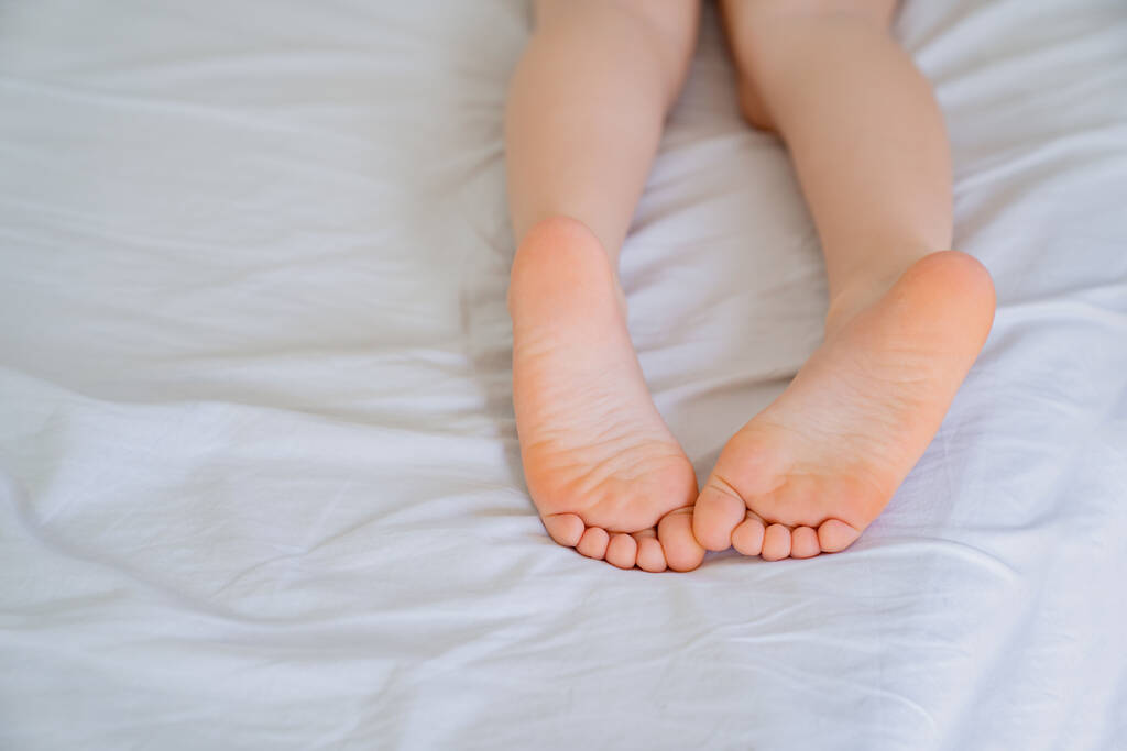 Çocuk bacakları yatakta. pembe ayaklar ve düz topuklar - Fotoğraf, Görsel