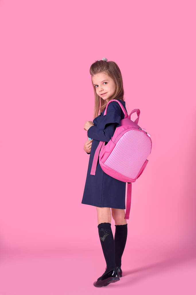 Επιστροφή στο σχολείο έννοια Μισή γύρισε φωτογραφία πορτρέτο της υπέροχη αυτοπεποίθηση όμορφο έξυπνο κορίτσι με τετράδιο copybook φορώντας σχολική στολή φόρεμα ροζ φωτεινό σακίδιο απομονωμένο - Φωτογραφία, εικόνα