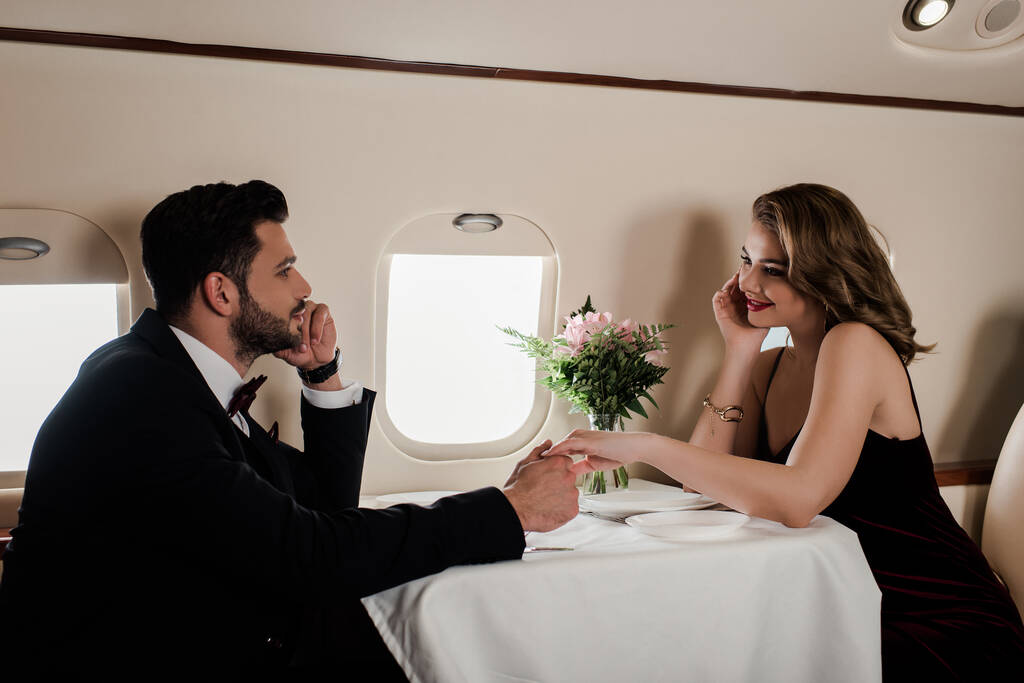 Uçakta servis masasında oturan zarif kadın ve erkek el ele tutuşuyor. - Fotoğraf, Görsel