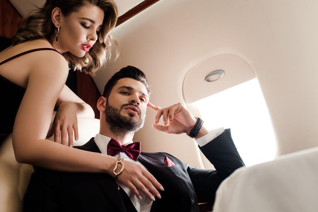Tiefansicht einer sexy Frau, die im Flugzeug die Brust eines eleganten, selbstbewussten Mannes berührt - Foto, Bild