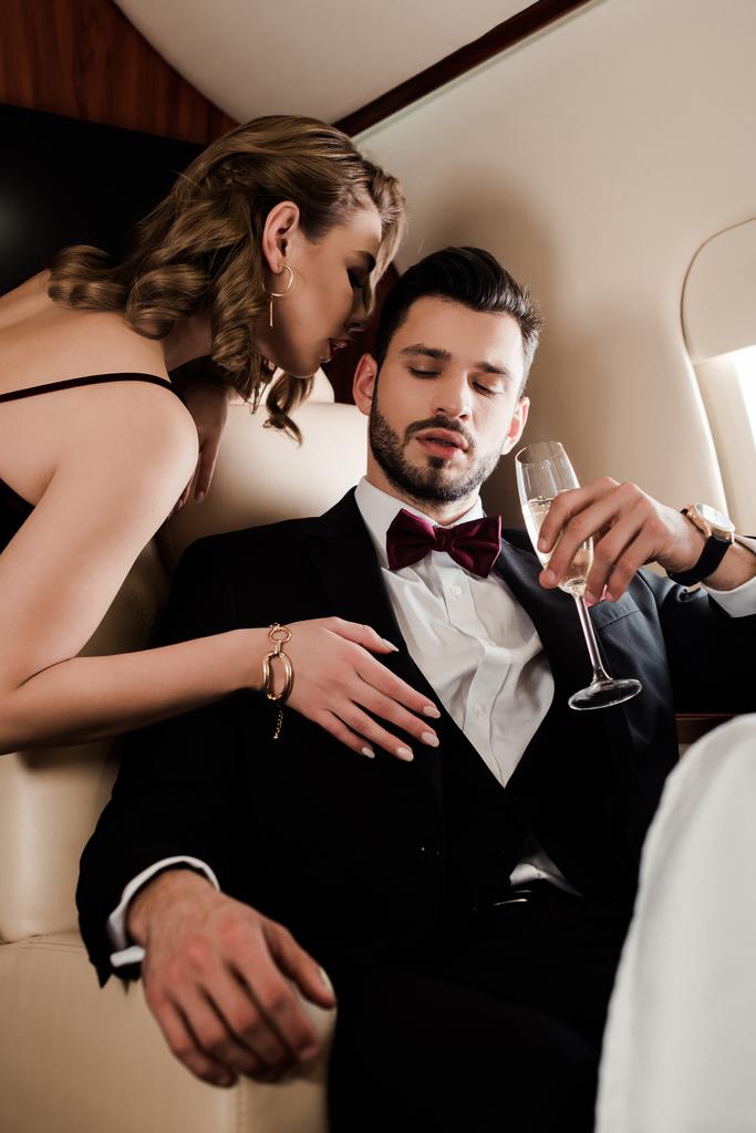 αισθησιακή γυναίκα αγγίζει κομψό άνδρα κρατώντας ένα ποτήρι σαμπάνια στο αεροπλάνο - Φωτογραφία, εικόνα