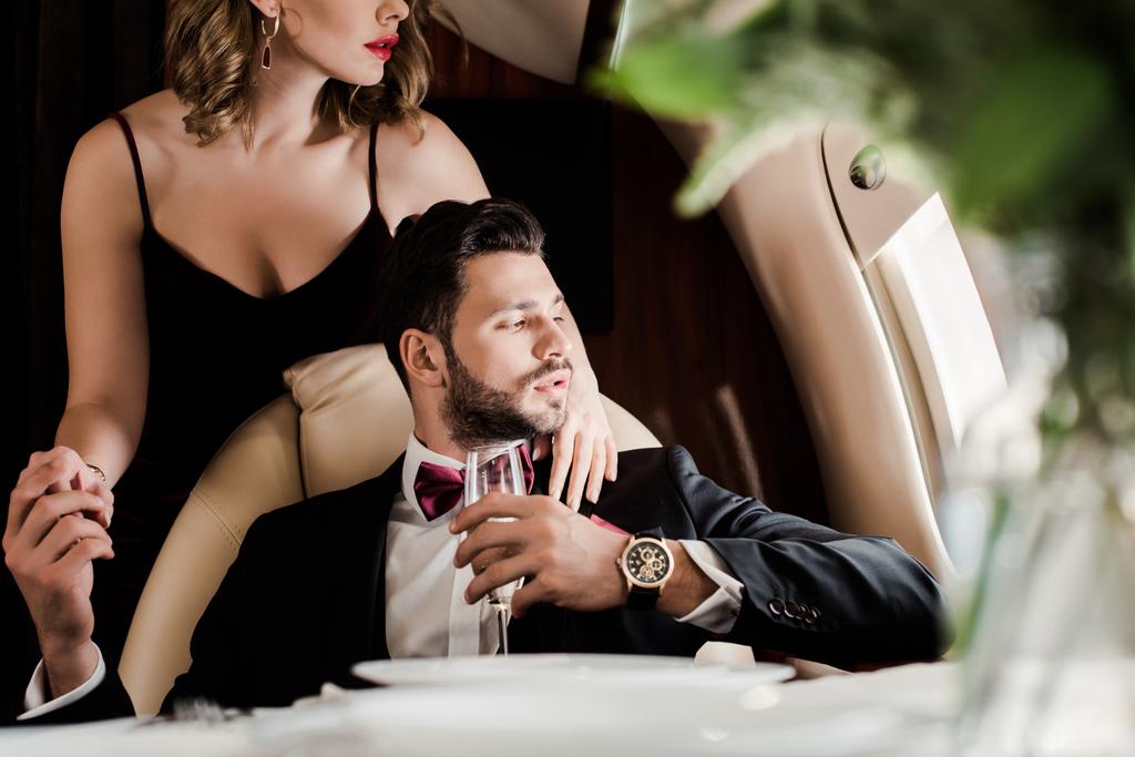 bijgesneden uitzicht van sexy vrouw aanraken elegante man holding glas champagne in vliegtuig - Foto, afbeelding