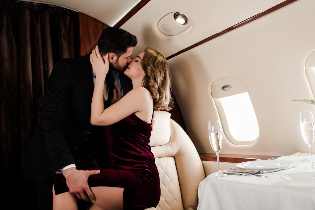 Όμορφος άντρας αγγίζει πόδι και φιλάει σαγηνευτική γυναίκα στο αεροπλάνο. - Φωτογραφία, εικόνα