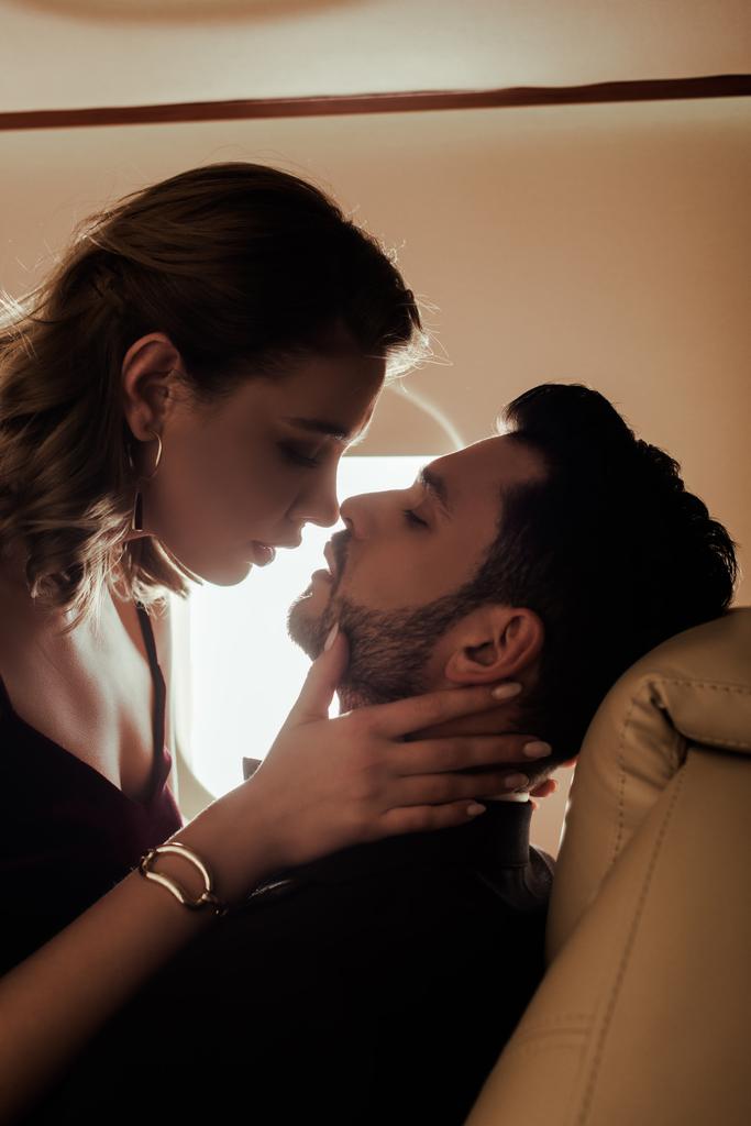 вид сбоку на сексуальную молодую женщину, трогающую лицо красивого мужчины в самолете
 - Фото, изображение